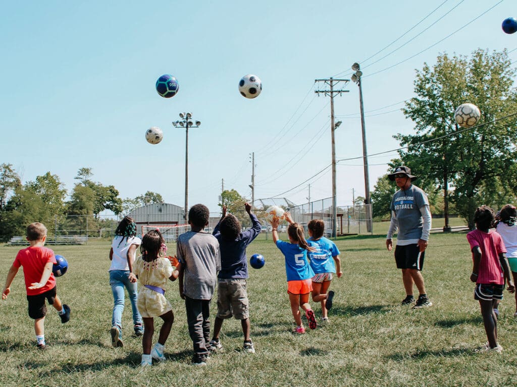 Kinder werfen Fußbälle in die Luft während eines Gemeindeprogramms mit Ambassadors Football Pittsburgh.
